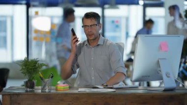 Arka planda çalışan meslektaşları ile modern ofis onun masasında cep telefonuyla konuşan işadamı.