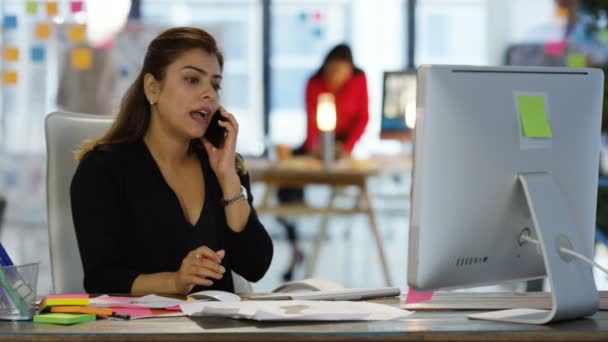 印度女商人在她的办公桌上谈论手机与同事在后台工作 — 图库视频影像