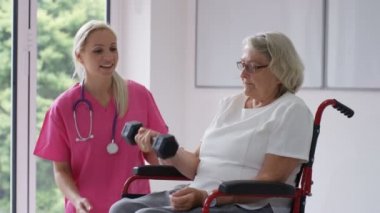 Yatılı bakım ev hemşire yaşlı Bayan tekerlekli sandalyede ağırlıklar ile bazı egzersizleri gösterilen.