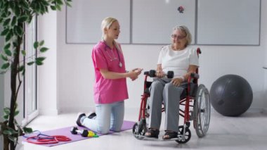 Yatılı bakım ev hemşire yaşlı Bayan tekerlekli sandalyede ağırlıklar ile bazı egzersizleri gösterilen.