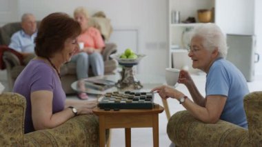 Bir huzurevi ve sakinleri dikkat çekici genç hemşire dama oynayan neşeli kadınlar.