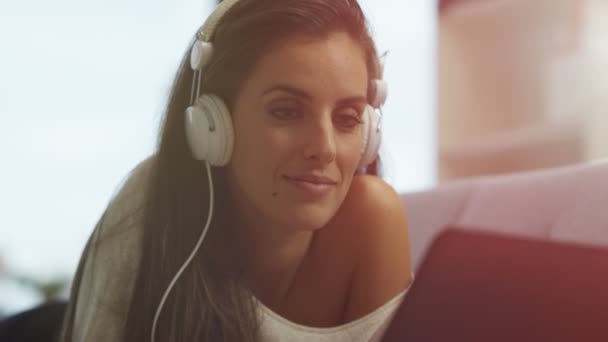美しい女性は家でのんびり ノート パソコンとヘッドフォンで音楽を聴く — ストック動画