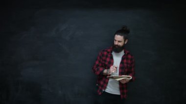 4k gülümsüyor not defterinde kara tahta arka plan üzerinde yazma hipster adam portresi