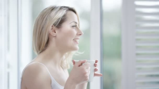 女性自宅でコーヒーのカップを楽しんでいると 窓の外を見て — ストック動画