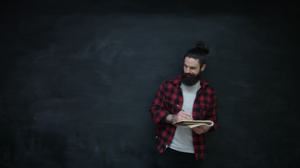 在黑板背景下的笔记本上思考时髦男士写作 — 图库视频影像