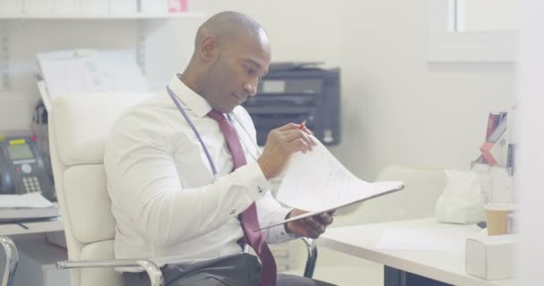 患者ノートに書いて事務所に座っている笑顔のドクターの肖像 — ストック動画