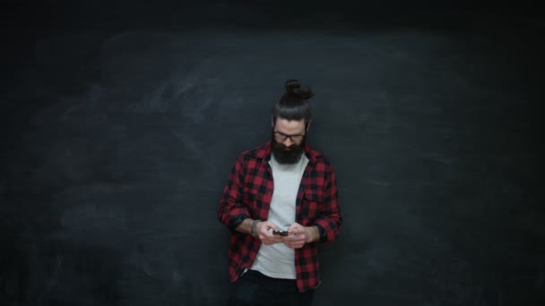 Smiling Hipster Uomo Guardando Lati Sopra Utilizzando Smartphone Sulla Lavagna — Video Stock