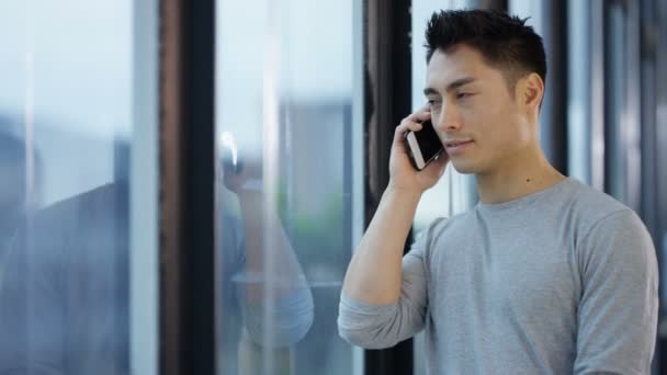亚洲商人站在窗口旁边 在城市办公室用手机交谈 — 图库视频影像