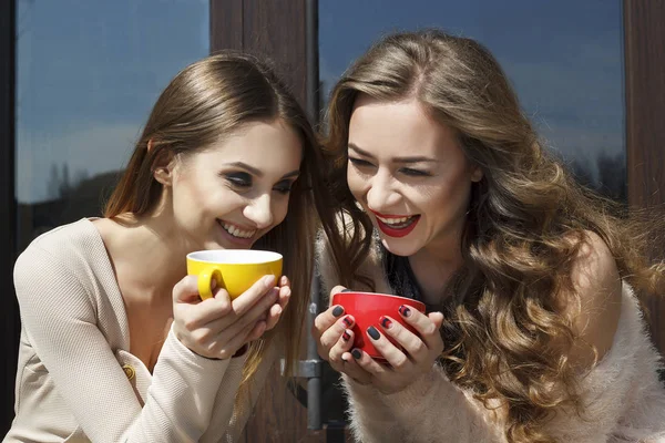 Dos mujeres hermosas jóvenes tomando café o té y riendo —  Fotos de Stock