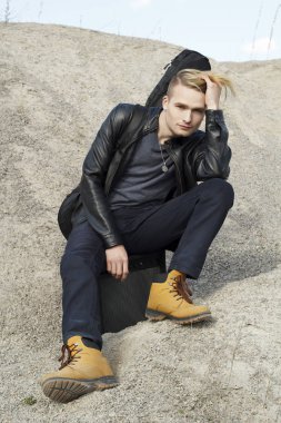 Kum üzerine oturan genç sarışın gitar çalan portresi.