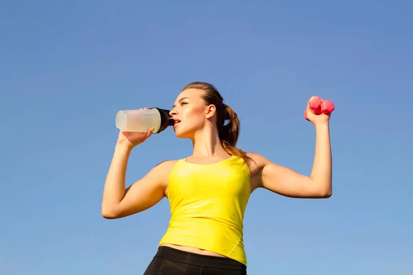 Young beautiful smiley woman doing sport exercises and drinking water outdoors — Stock Photo, Image