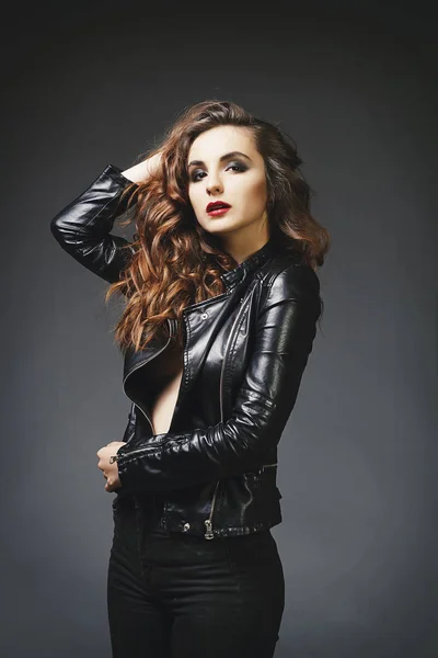 Beautiful young woman posing in leather jacket over grey backgro — Stock Photo, Image