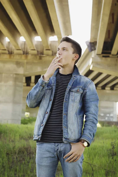 Joven atractivo hombre fumar al aire libre wering jeans ropa —  Fotos de Stock