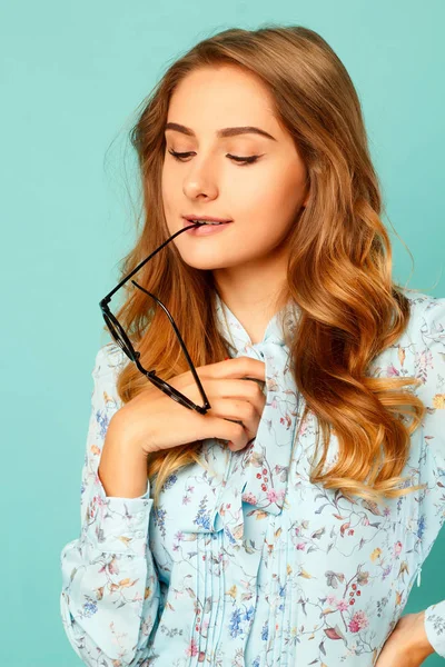 Ziemlich nachdenkliches Mädchen mit Brille im Mund über blauem Rücken — Stockfoto