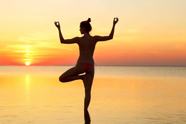 Jonge mooie brunette vrouw doen yoga bij zonsondergang op het strand — Stockfoto