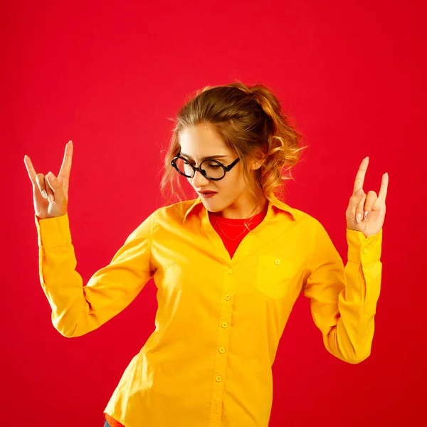 Joven mujer bonita divertida con el rock-n-roll gesto sobre el respaldo rojo —  Fotos de Stock