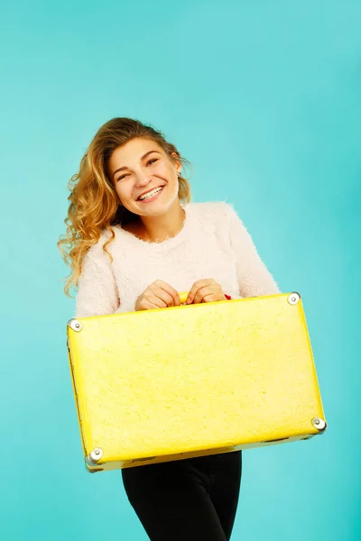 Joven feliz hermosa mujer sosteniendo maleta amarilla sobre azul ba —  Fotos de Stock
