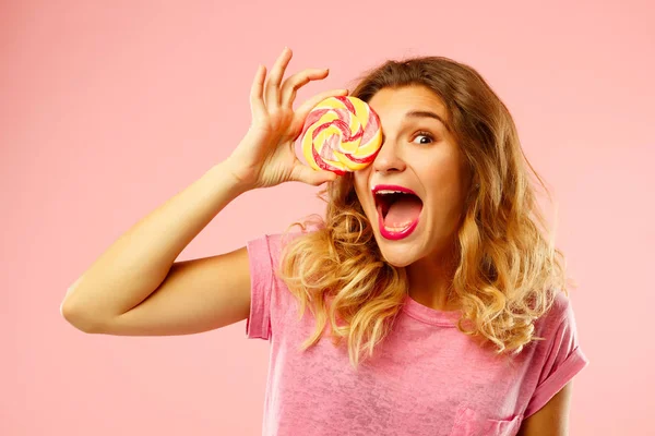 Porträt eines glücklichen hübschen Mädchens, das süße Bonbons über rosa Ba hält — Stockfoto