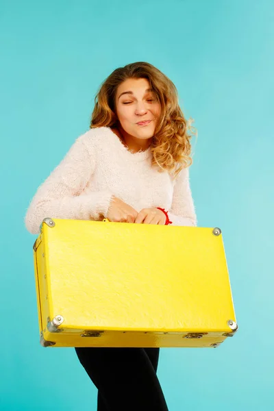 Jeune jolie femme heureuse tenant une valise jaune sur fond bleu — Photo