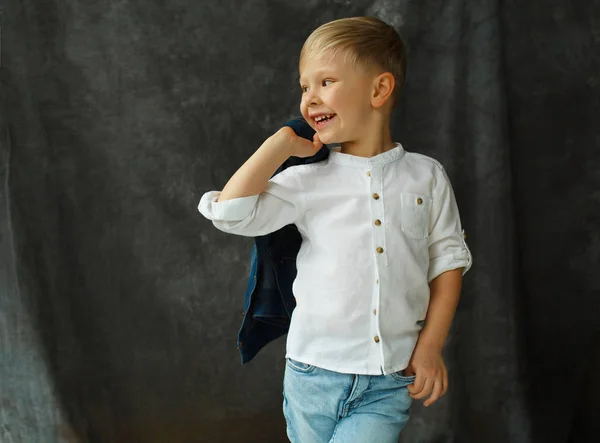 Portrait of little smiley pretty boy in jeans over grey textile — Stock Photo, Image