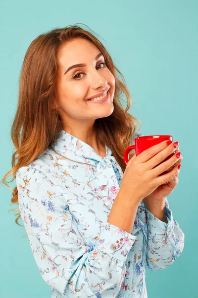 Giovane donna che tiene una tazza di tè o caffè su sfondo blu — Foto Stock