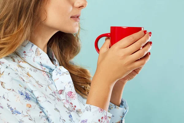 Молодая женщина держит чашку чая или кофе на синем фоне — стоковое фото
