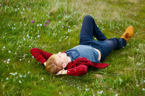 Immagine di giovane bellissimo uomo biondo sdraiato su erba verde tra — Foto Stock