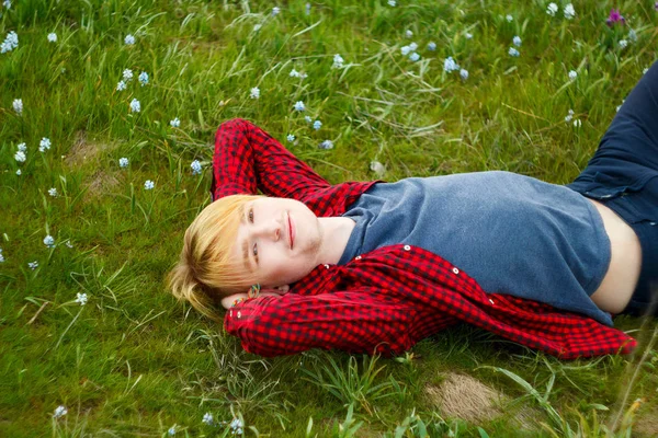 Фото молодого красивого блондина, лежащего на зеленой траве среди — стоковое фото