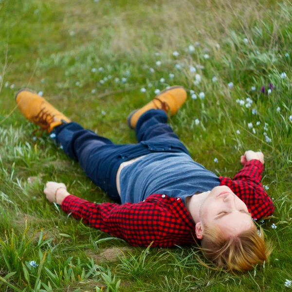 Imagem de jovem homem loiro bonito que coloca na grama verde entre — Fotografia de Stock