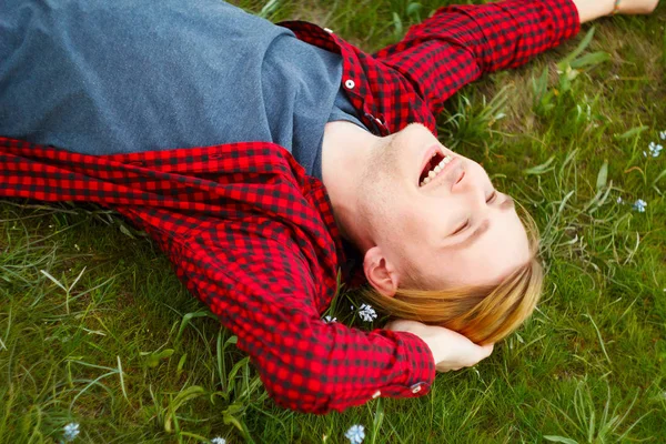 Immagine di giovane bellissimo uomo biondo sdraiato su erba verde tra — Foto Stock