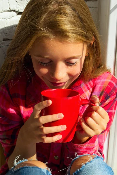 Портрет маленькой милой улыбчивой девушки с чашкой в руках, пьющей — стоковое фото