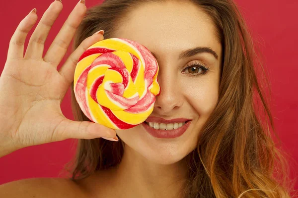 Portrét hezká dívka drží sladké cukroví nad červeným poza — Stock fotografie