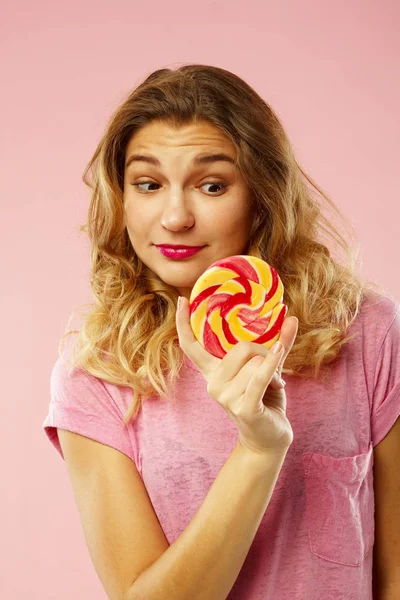 Портрет счастливой красивой девушки, держащей сладкие конфеты над розовым ba — стоковое фото