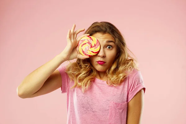 Porträt eines glücklichen hübschen Mädchens, das süße Bonbons über rosa Ba hält — Stockfoto