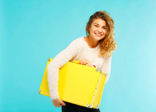 Joven feliz hermosa mujer sosteniendo maleta amarilla sobre azul ba —  Fotos de Stock