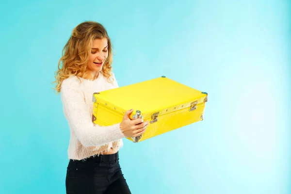 Joven hermosa mujer sosteniendo maleta amarilla sobre fondo azul —  Fotos de Stock