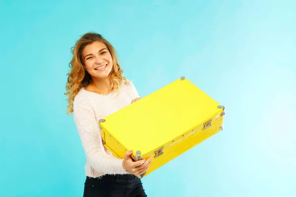 Joven hermosa mujer sosteniendo maleta amarilla sobre fondo azul —  Fotos de Stock