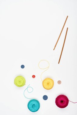 Colorful threads, multi-colored buttons and crochet hooks on a white surface. Top view.