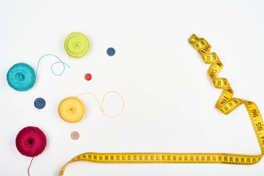 Colorful threads, multi-colored buttons and tape measure on a white surface. Top view.