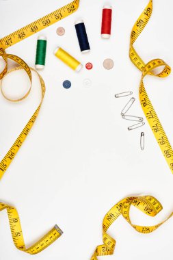 Multi-colored threads and buttons, tape measure and pins on a white surface. Top view.