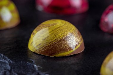 Handmade candies in colored glaze on a black chalkboard. Close-up.