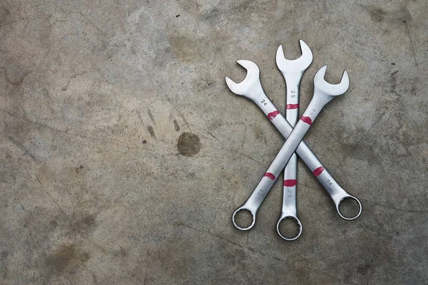 Crossed chrome wrenches on concrete floor.