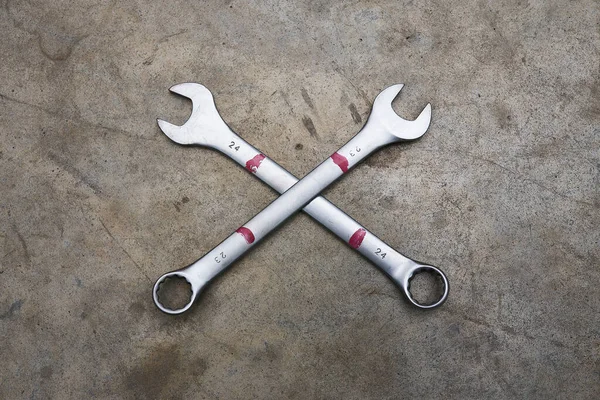 Two wrenches lying crossed like bones on concrete floor.