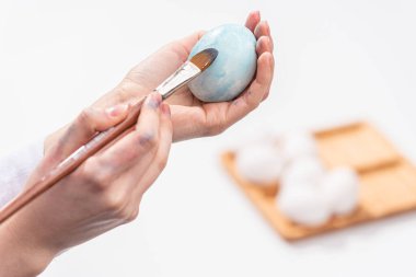 Paskalya kutlaması. Ev yapımı yumurta boyama geleneği. Kadın fırçayla Paskalya yumurtası boyuyor. Beyaz arka plan. Yakın plan..