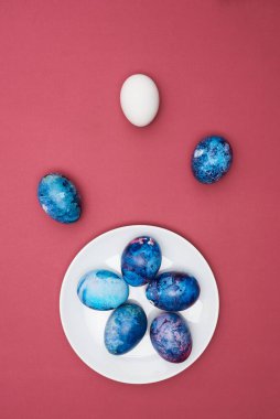 Bir tabakta renkli yumurtalar boyadım. Mor arka plan. Üst görünüm.