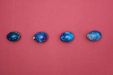 Mutlu Paskalyalar. Bordo bir yüzeye mavi boyanmış Paskalya yumurtaları.