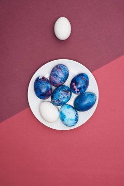 Paskalya bayramı, beyaz tabakta boyanmış yumurtalar. Mor arka plan. Üst görünüm.