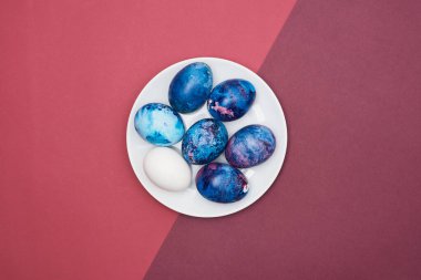 Beyaz bir tabakta renkli bir arka planda Paskalya bayramı yumurtaları. Üst görünüm.