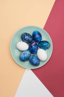Mutlu Paskalyalar. Renkli arka planda mavi bir tabakta Paskalya bayramı yumurtaları. Üst görünüm.