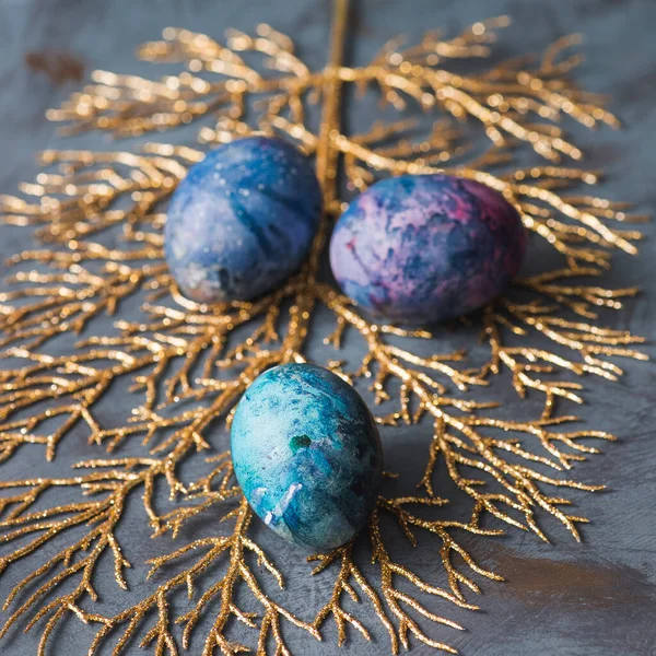 Easter holiday. Easter eggs on a golden branch. Blue background. Close-up.